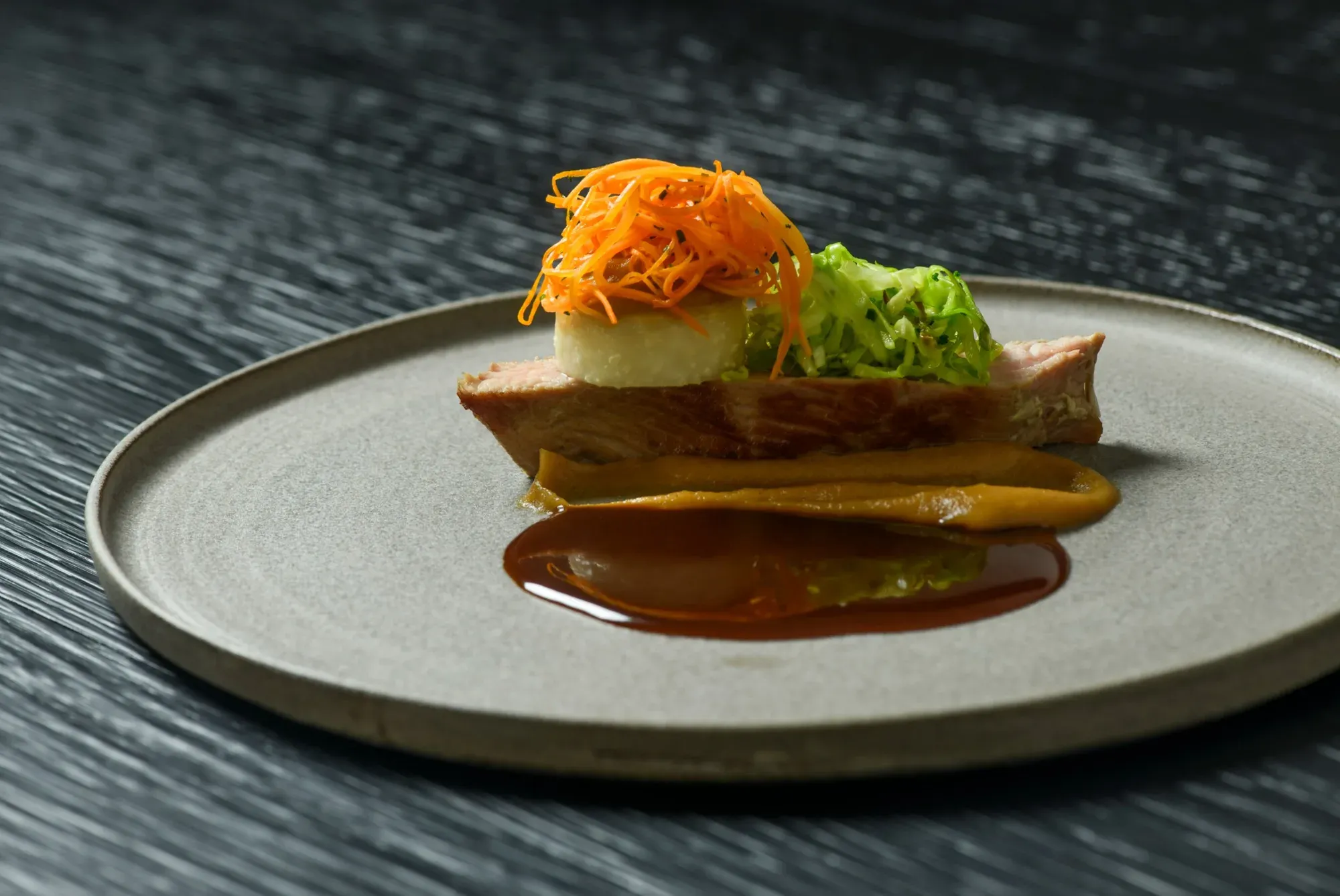 A main course with sauce and vegetables on a grey plate at the Chef's Table by Gesser