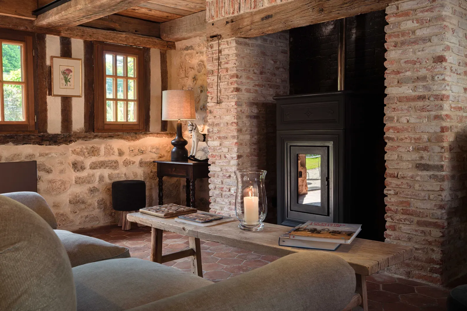 The sitting room of La Grande Forge with exposed brick, timber beams and a wood-burning stove