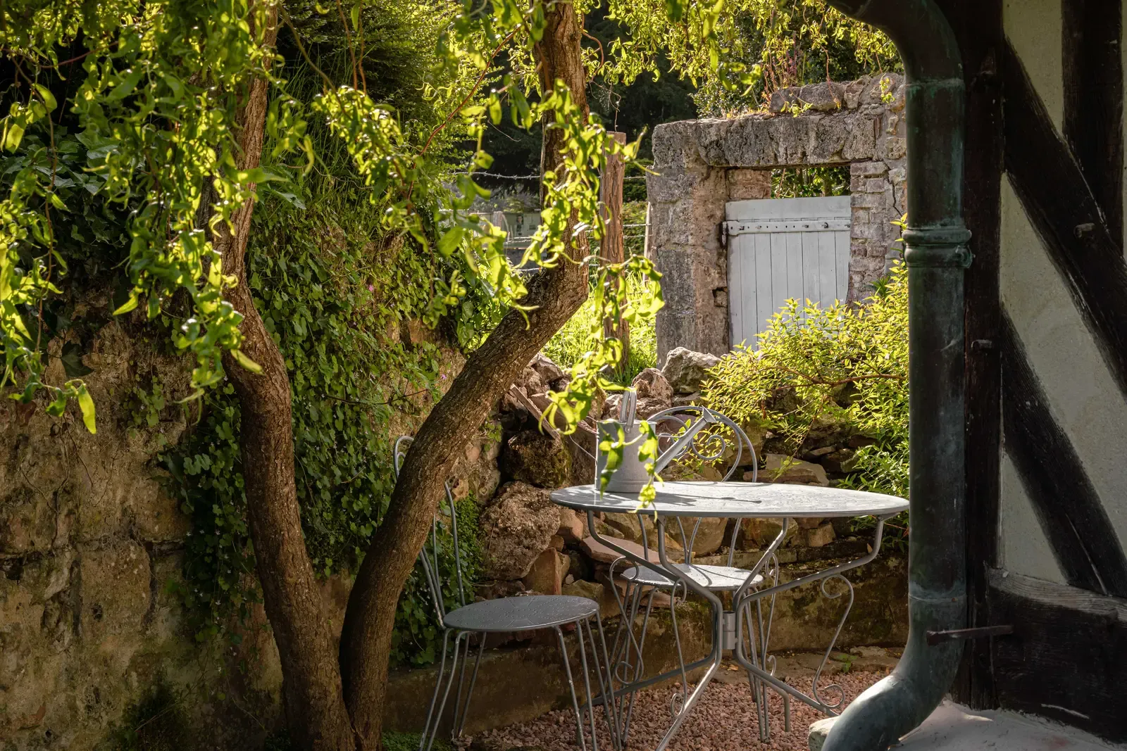 A small walled garden with a table and chairs under a tree at La Petite Forge
