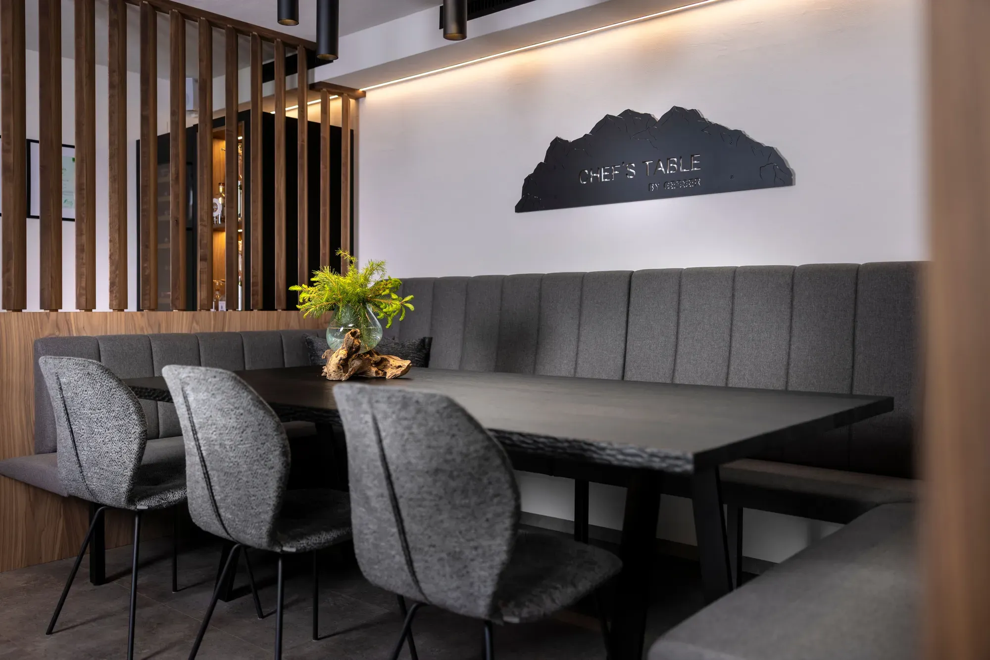 The Chef's Table by Gesser, a long table with grey chairs and the restaurant's mountain-shaped sign
