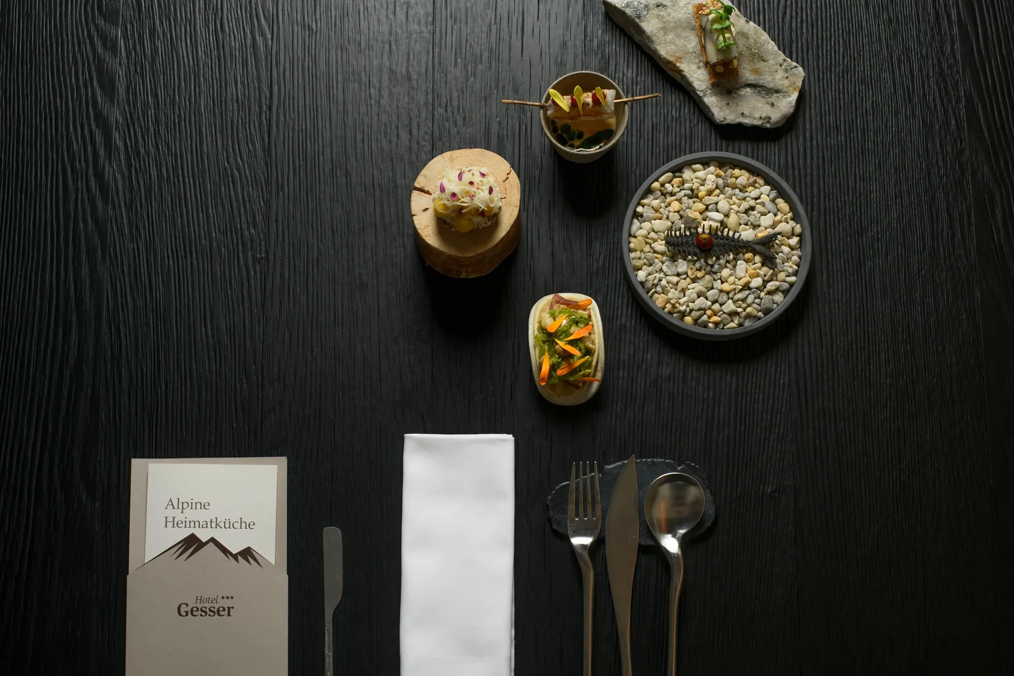 Small courses and the Alpine Heimatküche menu on a dark table at Chef's Table by Gesser