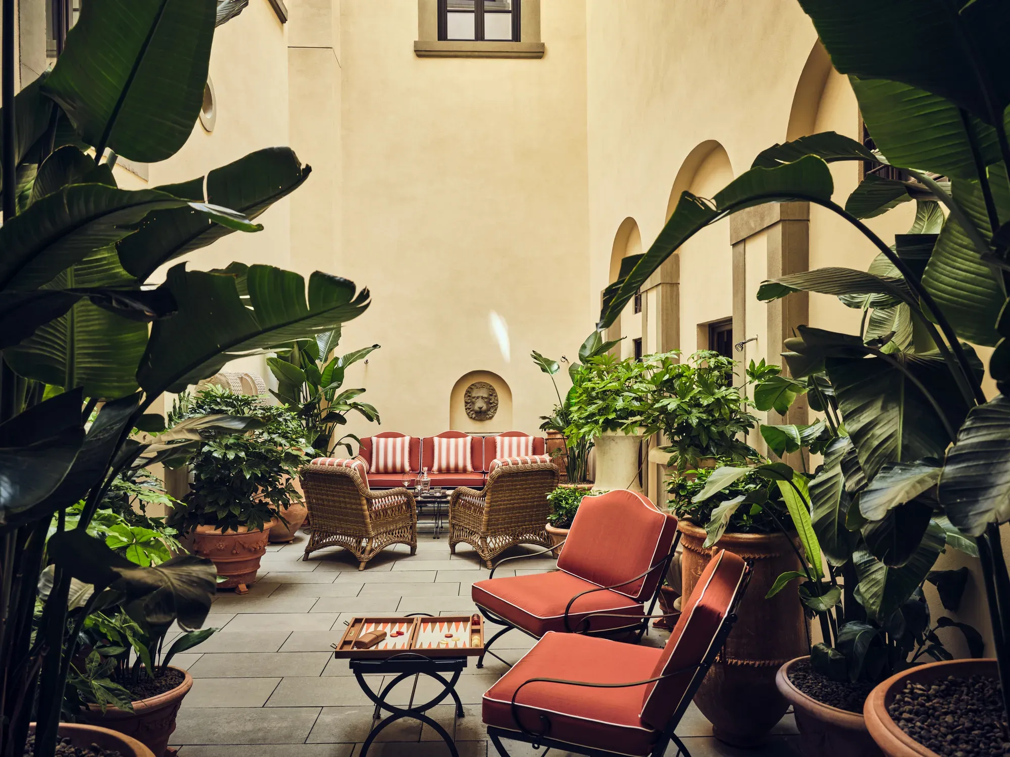 The shaded inner courtyard of La Réserve Firenze with red armchairs and plants