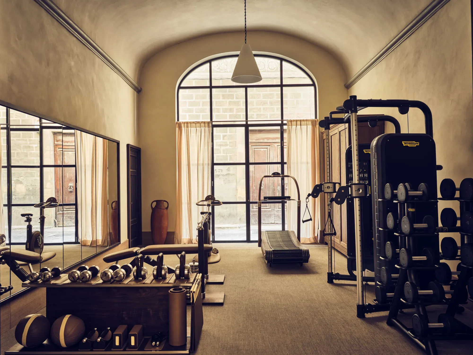 The gym of La Réserve Firenze under a vaulted window
