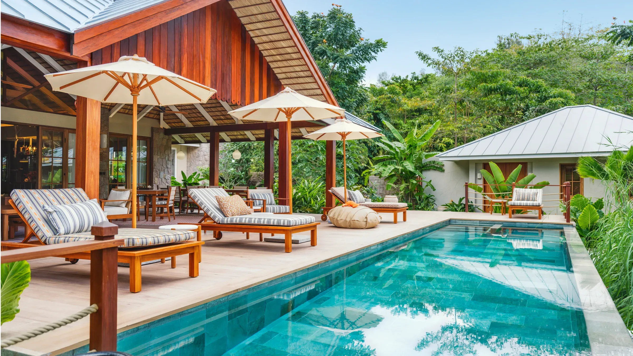 The pool deck of a private villa at La Réserve Seychelles on Praslin, with sun loungers, parasols and tropical garden