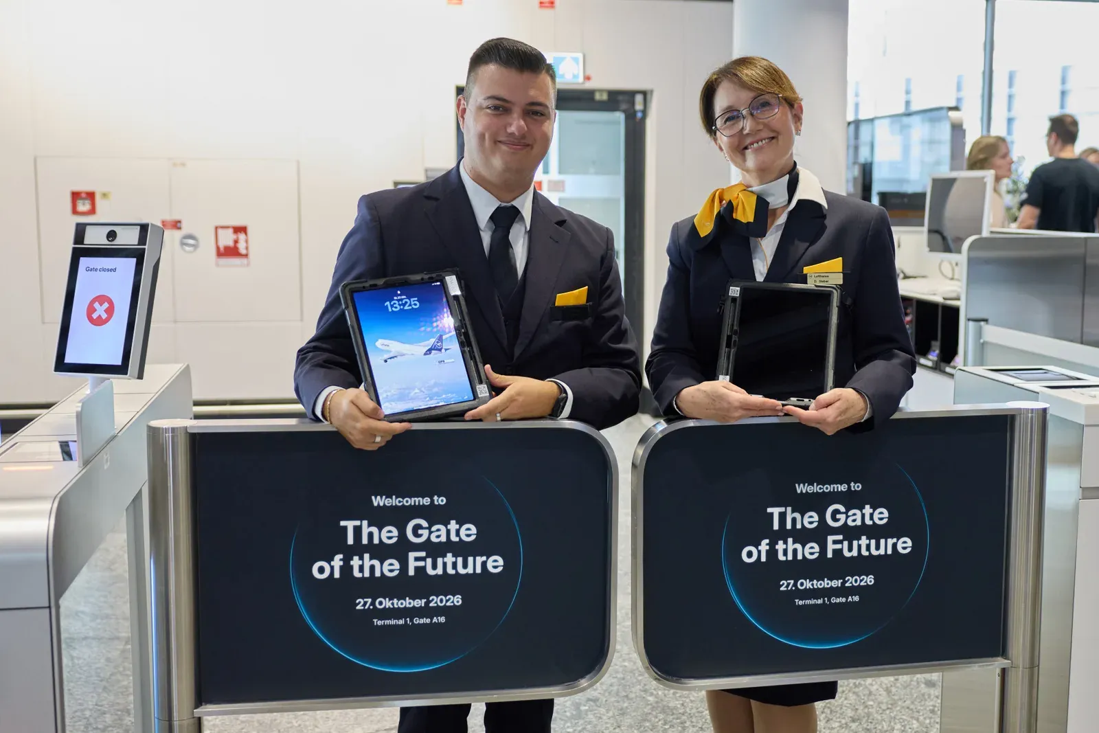 Two Lufthansa ground staff members with tablets behind the welcome signs of the Gate of the Future