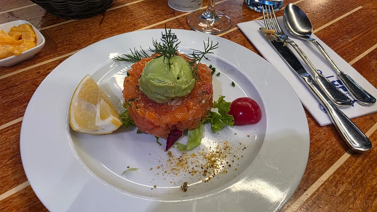 Salmon tartare with an avocado cream quenelle, dill, lemon and a cherry tomato on a Fisch Witte plate