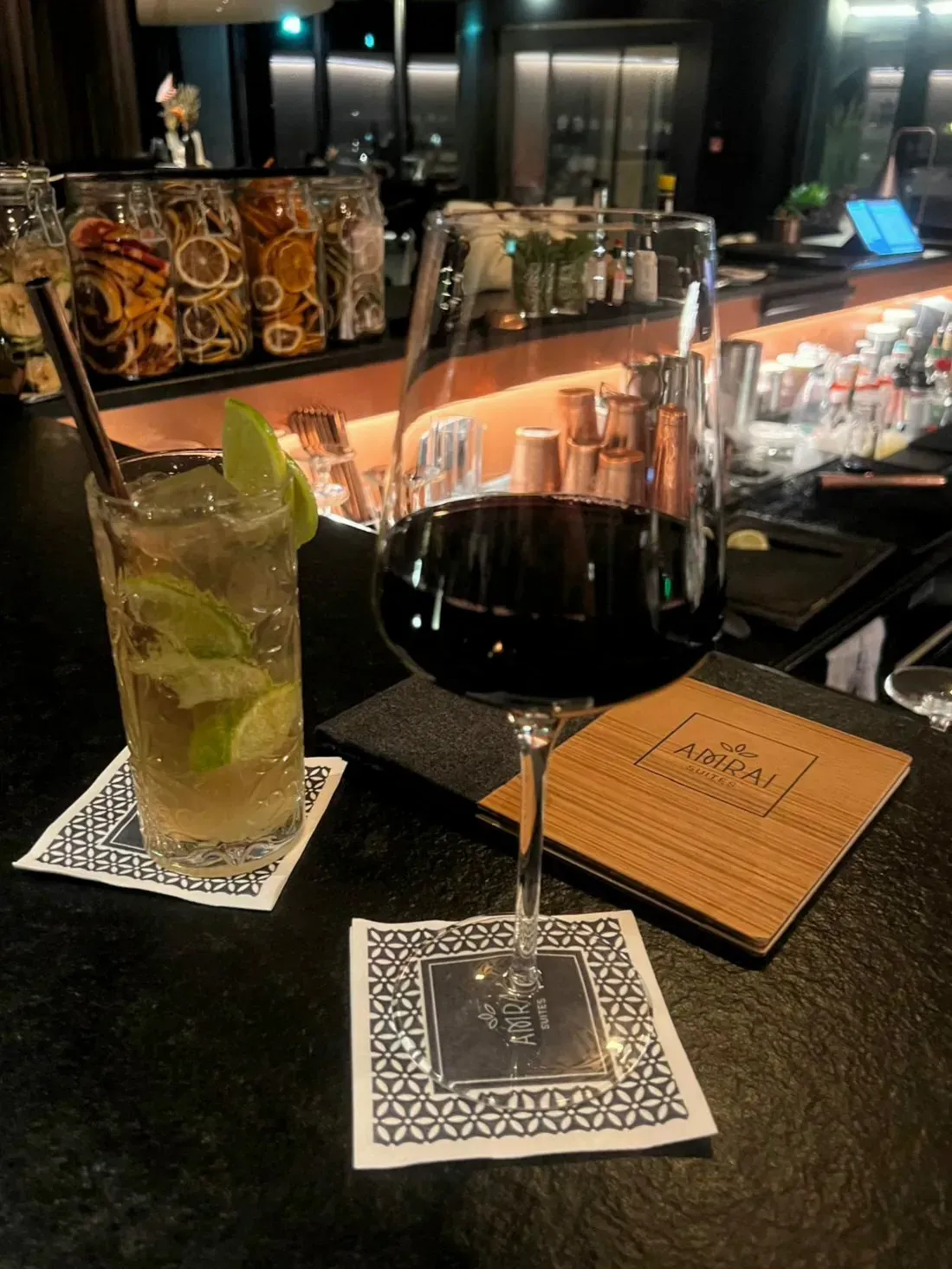 A long drink with lime and a glass of red wine at the AMRAI Bar in Schruns, with jars of dried citrus slices behind the counter
