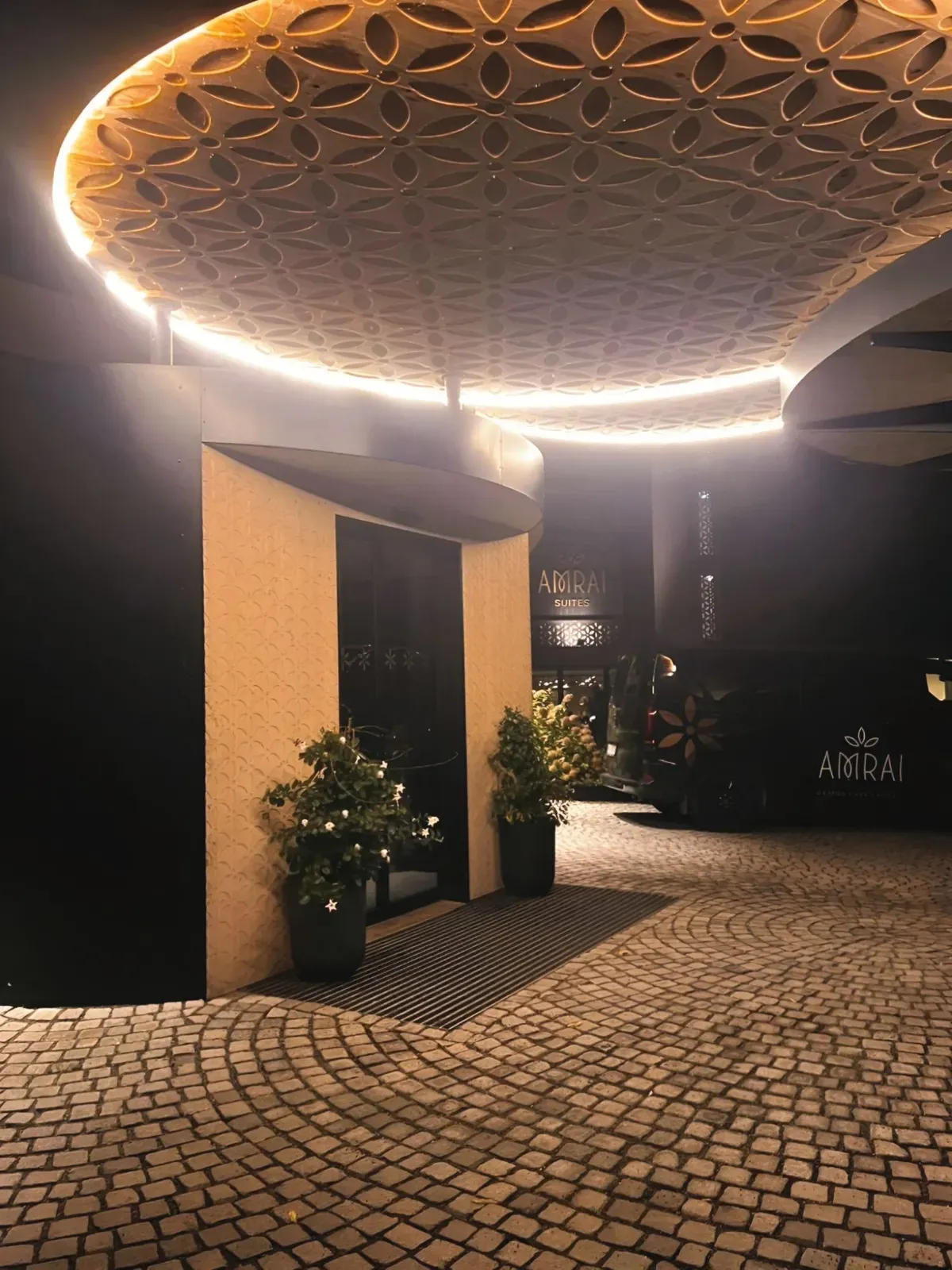The illuminated entrance of AMRAI Suites in Schruns at night, with its ornamented canopy and cobblestones