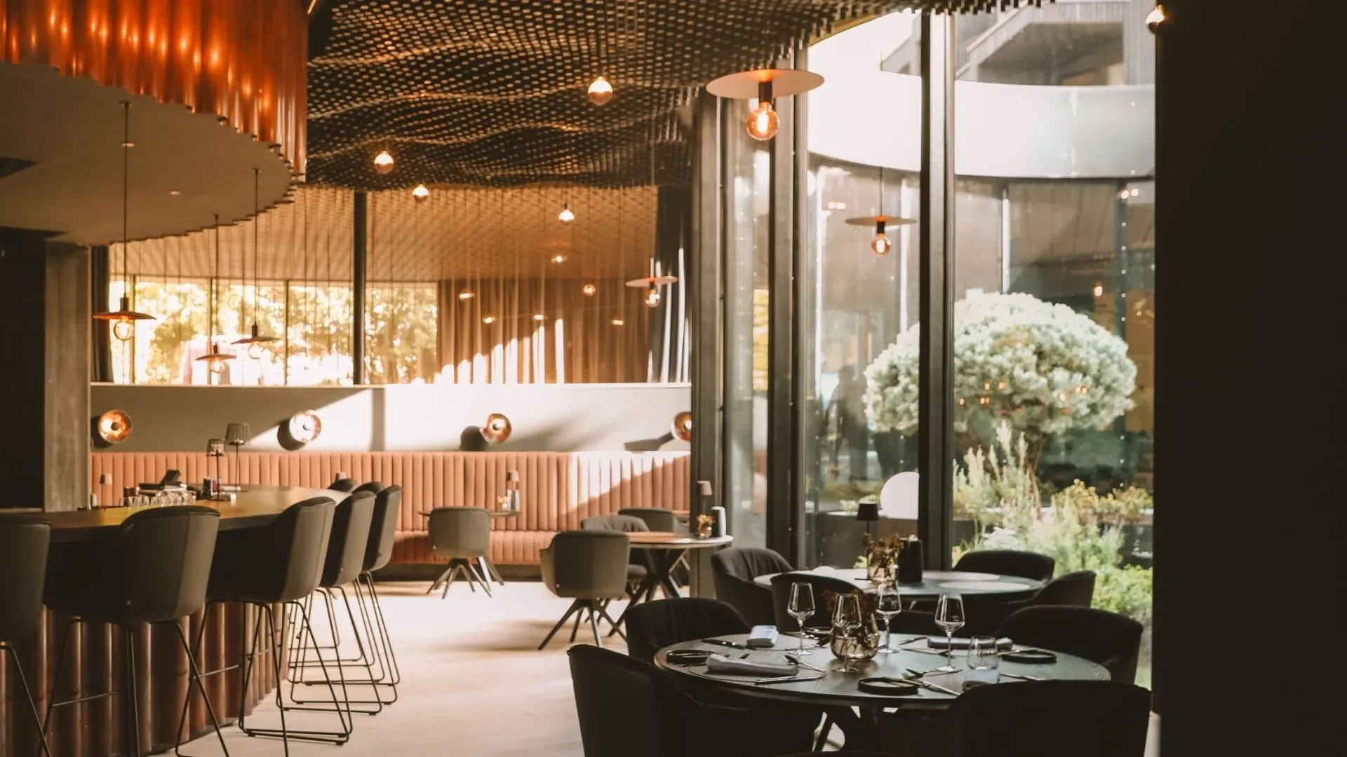 The Kupfrgrill at AMRAI Suites in daylight, with the copper-coloured rods, the bar seats and the garden beyond the glass