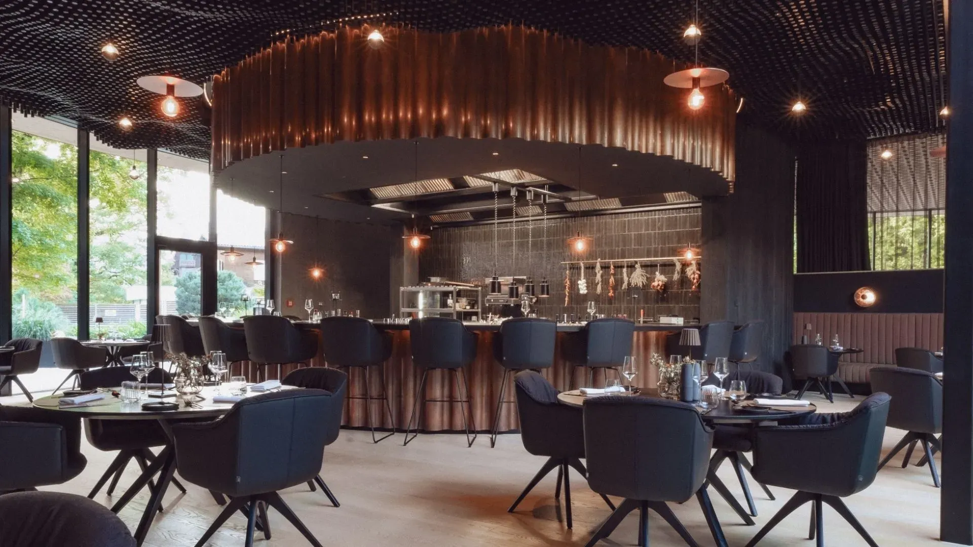 The Kupfrgrill dining room at AMRAI Suites with its open kitchen under a ring of copper-coloured rods
