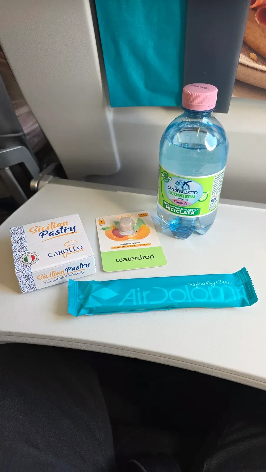 San Benedetto mineral water, a Carollo Sicilian Pastry, a Waterdrop peach ice tea cube and an Air Dolomiti refreshing towel at the Business Class seat