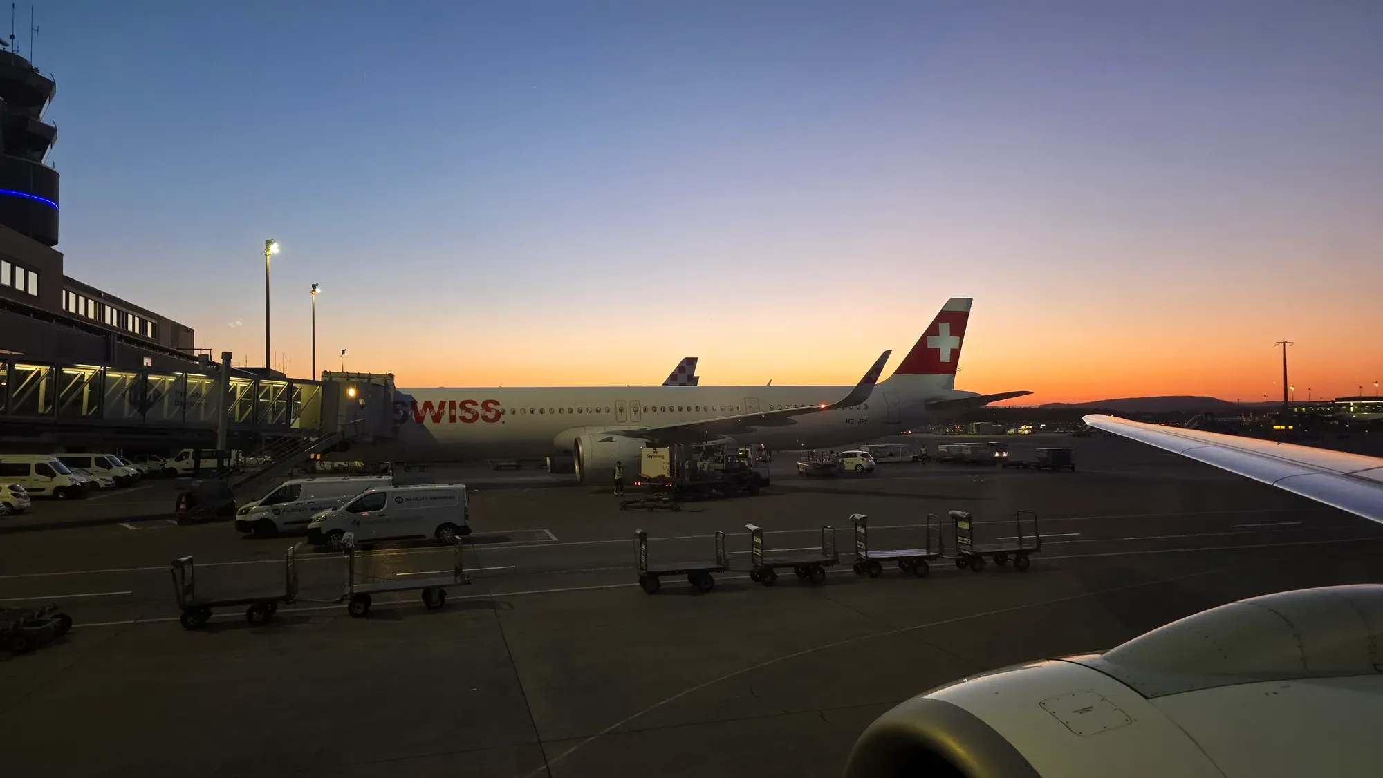 A SWISS Airbus A321neo at the gate at Zurich Airport at dusk, seen from the Helvetic E195-E2
