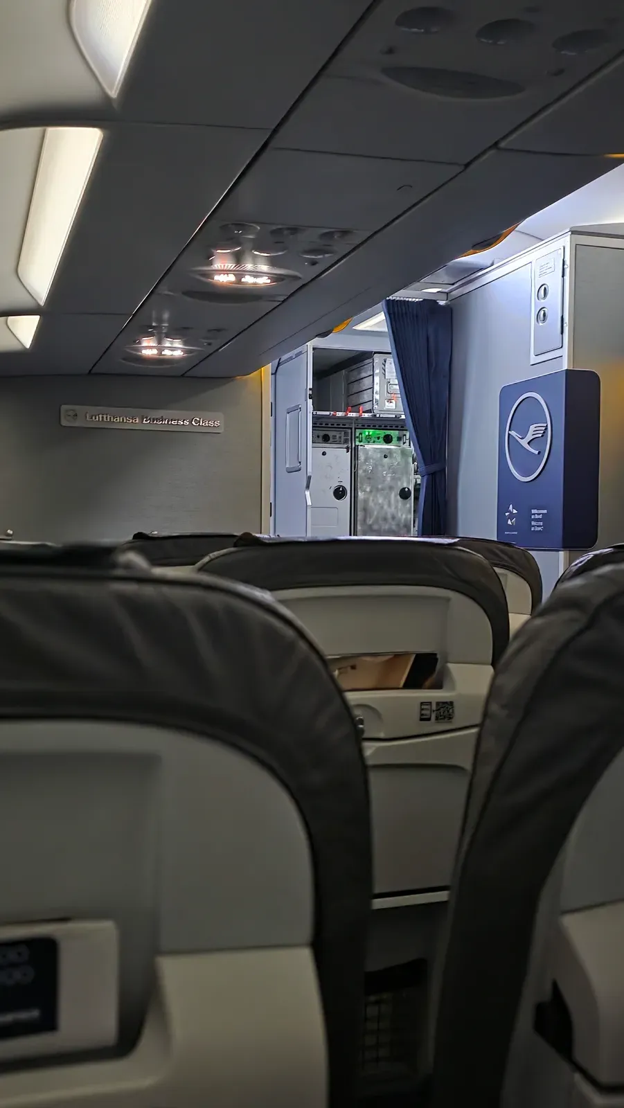 The Business Class cabin of the Lufthansa A321 with the Lufthansa Business Class sign and the welcome panel at the front