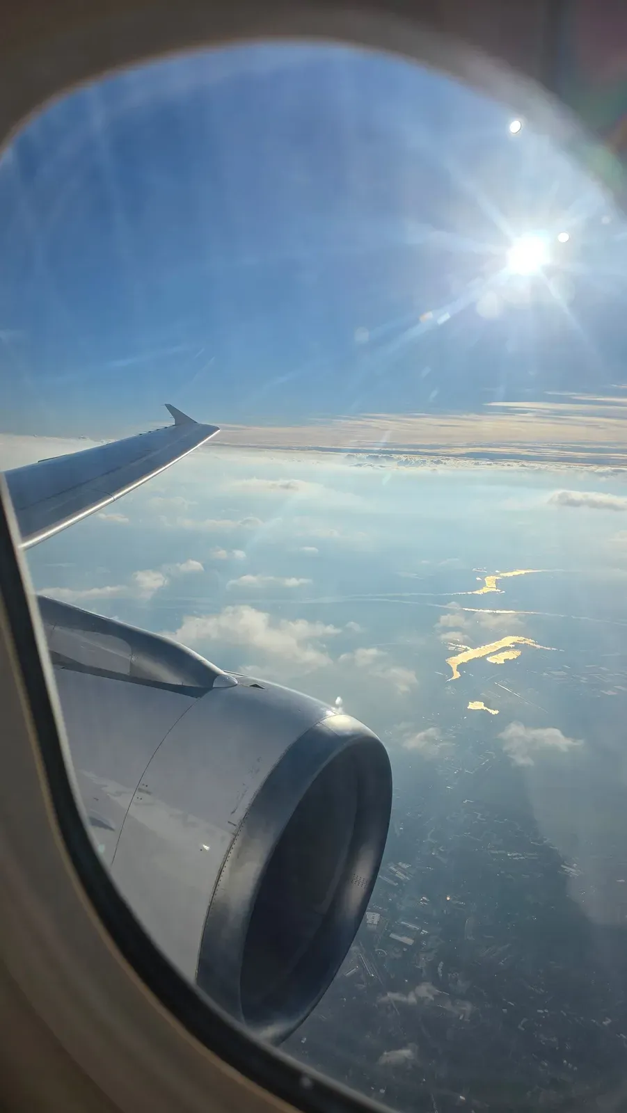 Sun above the clouds and lakes glinting below the wing of the SWISS A320 on the way to Hamburg