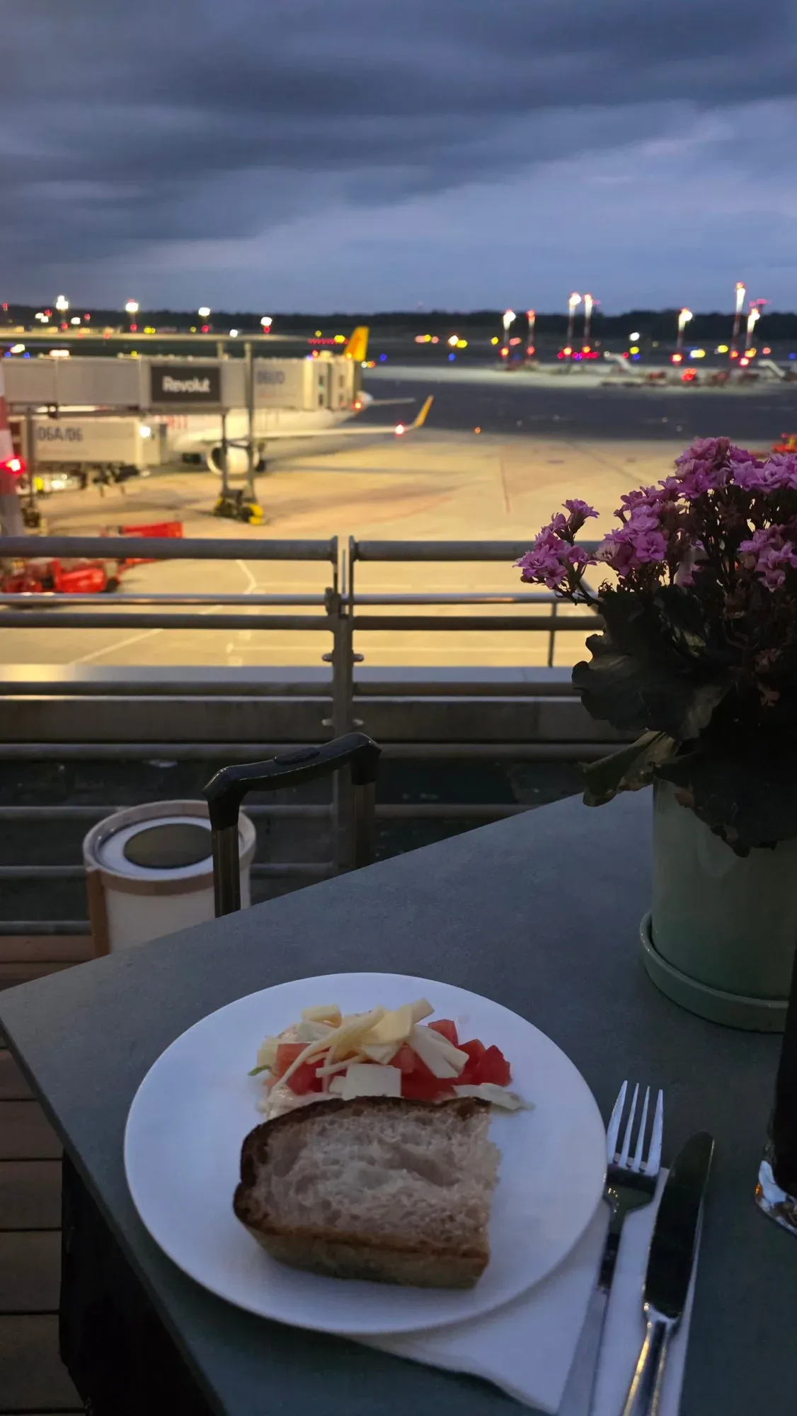Bread with tomato and cheese on the Senator Lounge terrace at dusk, with the apron lights of Hamburg Airport