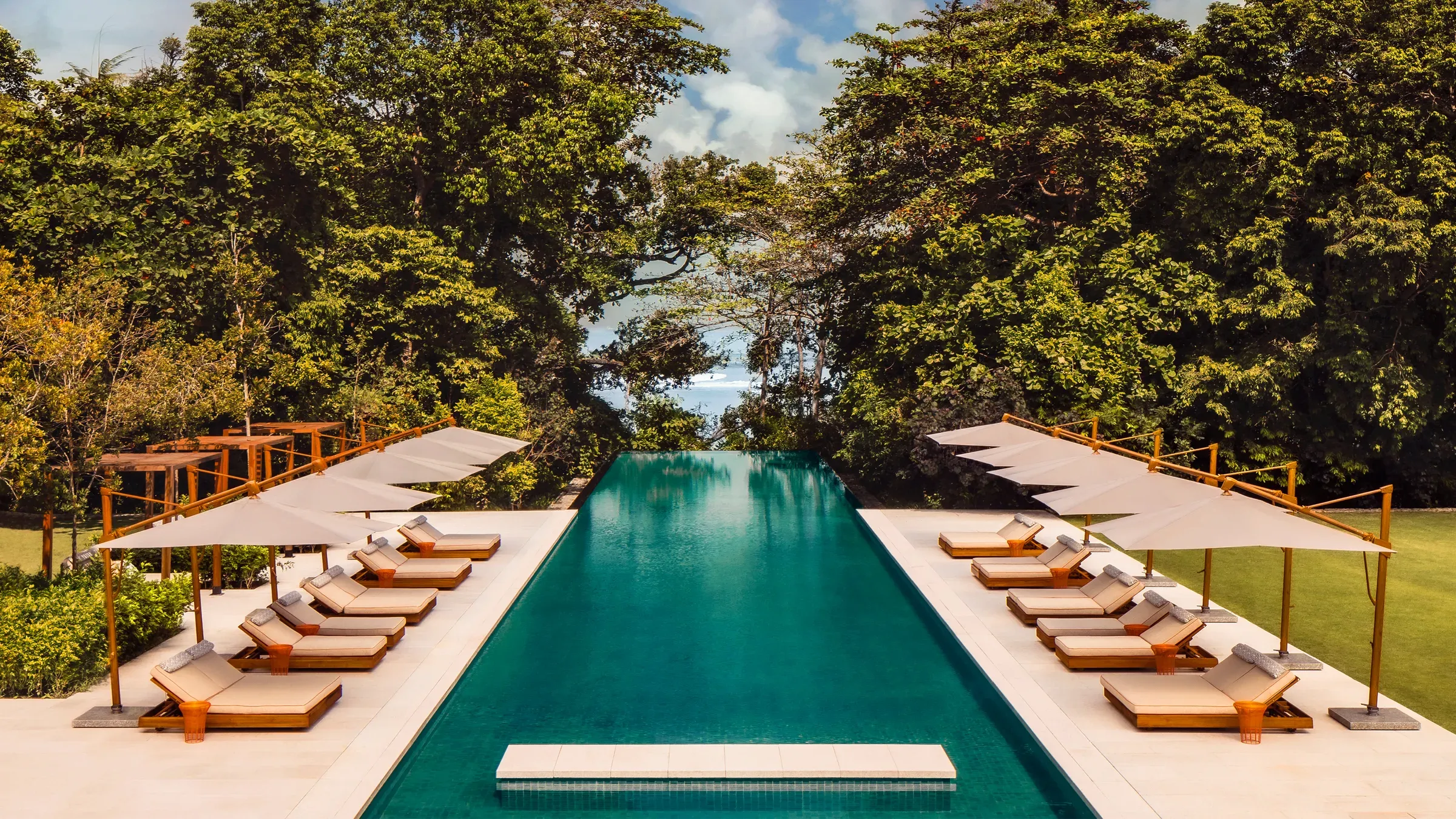 The long pool of Mandarin Oriental, Desaru Coast, lined with loungers and parasols and framed by rainforest
