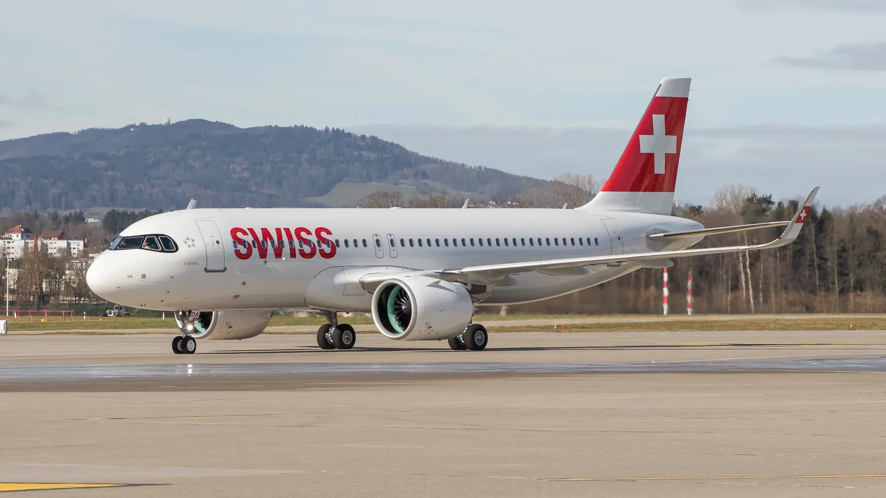 A SWISS Airbus A320neo taxiing at Zurich Airport with wooded hills in the background