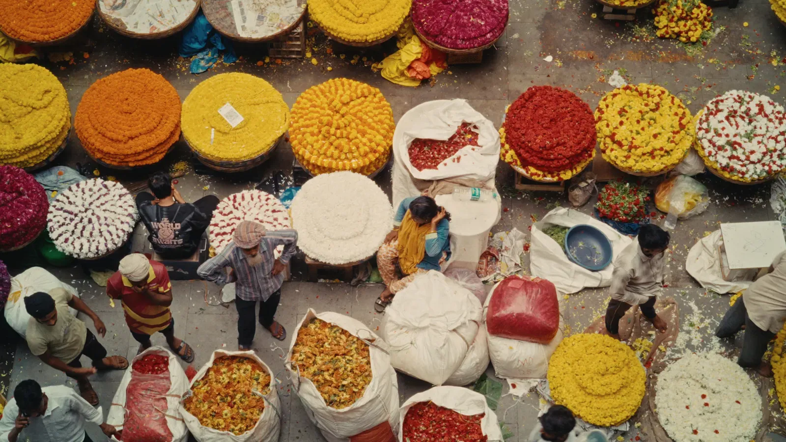 A bird's-eye view of flower sellers and piles of marigold garlands at a market in Bengaluru