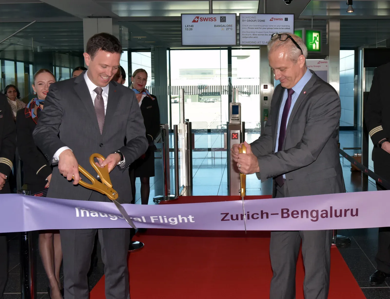 Jens Fehlinger and Simon Bosshart cutting a ribbon reading "Inaugural Flight Zurich–Bengaluru" at the gate in Zurich