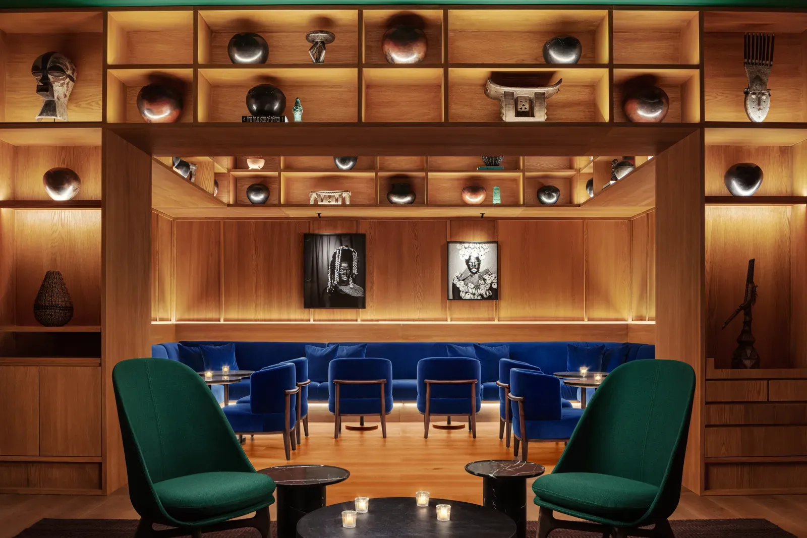 The Punch Room at The Cape Town EDITION with green armchairs, blue banquettes and shelves of African craft